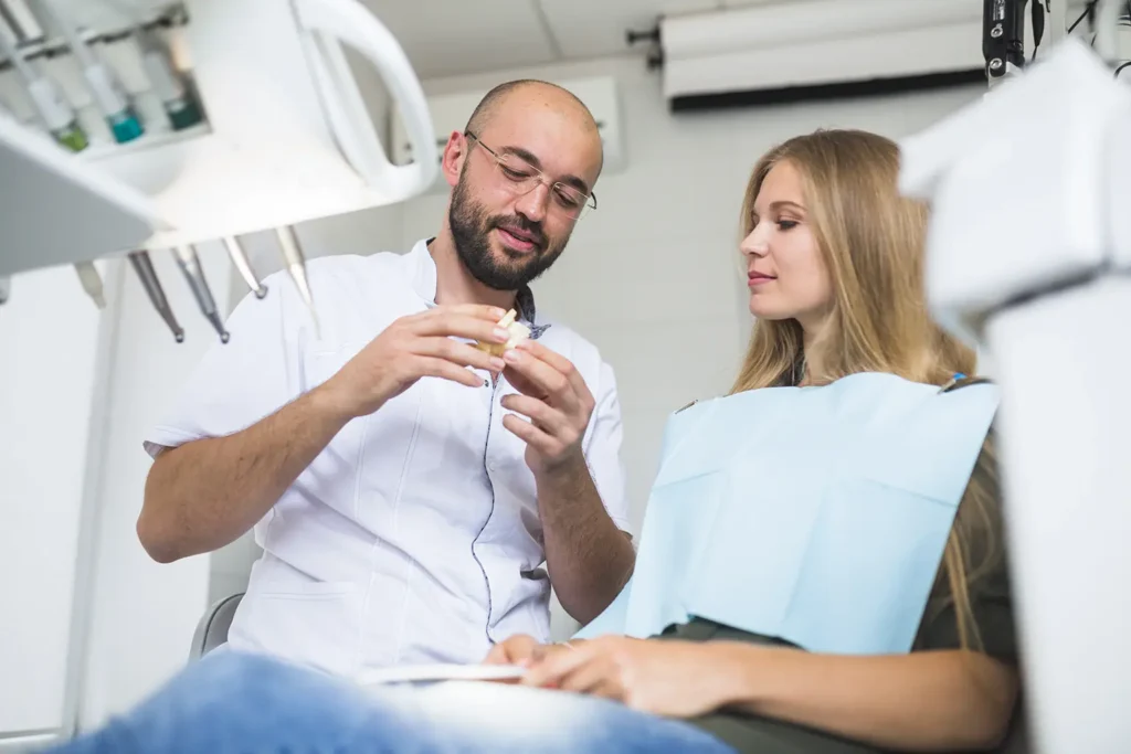 A dentist shows a dental model to a female patient in a clinic, highlighting ways to reduce dental expenses with the Rubicare Dental Savings Plan.